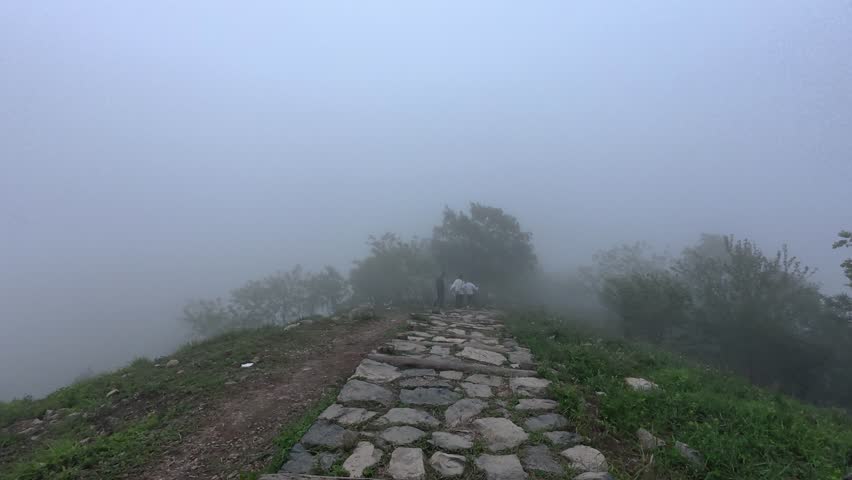 This image shows a rough stone paved hiking trail on a misty mountain ridge, with obscured trees and muted foggy atmosphere surrounding the path.