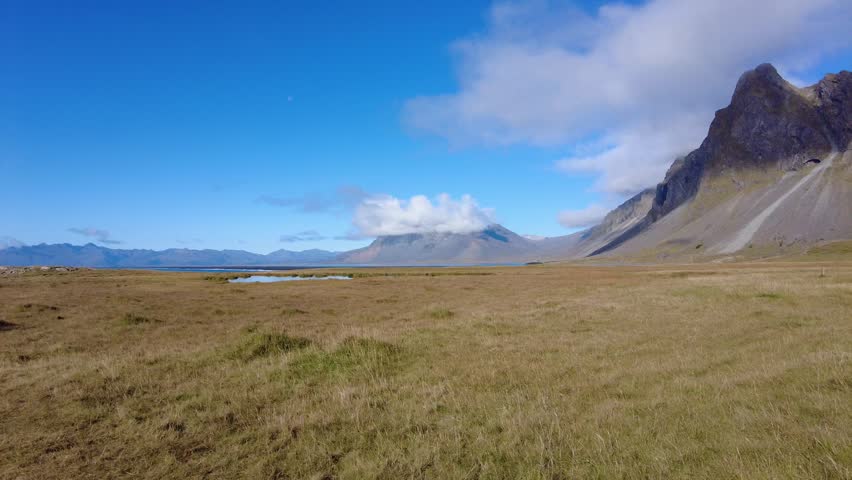 Icelandic Landscape with Sharp Mountain Peak and Grassy Tundra - Majestic Icelandic scenery featuring a jagged mountain peak rising above a vast grassy plain under a clear blue sky with drifting clouds.