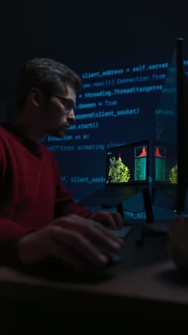 Focused data scientist writing code on keyboard in a dimly lit workspace in front of multiple monitors, with running programming script lines casting a blue glow across the dark office. Space for text