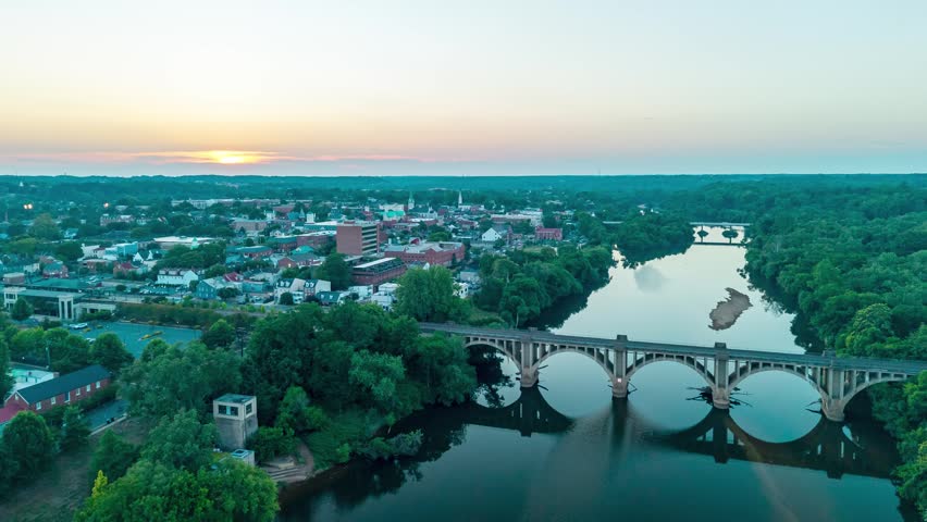 Fredericksburg, Virginia, stunning 4K aerial hyperlapse video flying over the Rappahannock River and historic concrete railroad bridge toward the downtown cityscape at sunset