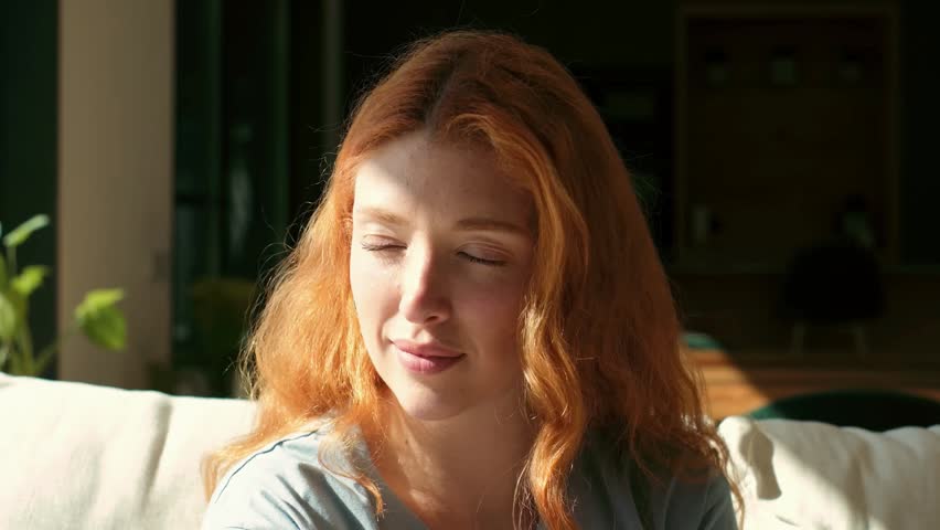 Beautiful Red-Haired Woman Enjoying Serene Morning Light While Relaxing on Her Couch