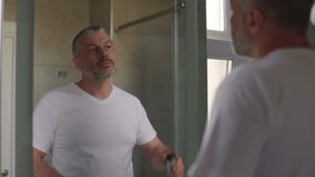 Middle aged man shaving beard with electric razor in front of mirror in bathroom 4k - Powered by Shutterstock - Get 15% off with code: PIKWIZARD15