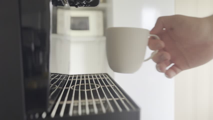 A person places a white mug under an automatic coffee machine nozzle.