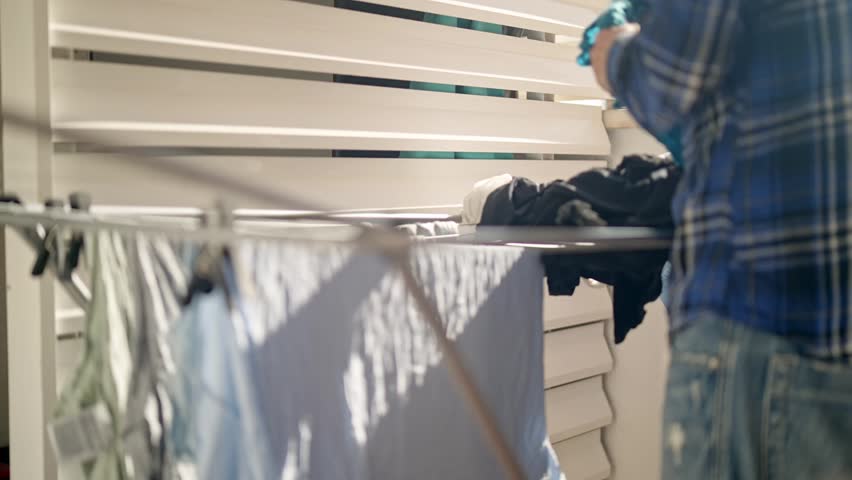 In this cozy setting along the Villajoyosa coast of Spain, a person hangs freshly washed clothes on a drying rack outside. The sun shines bright as items are carefully placed.