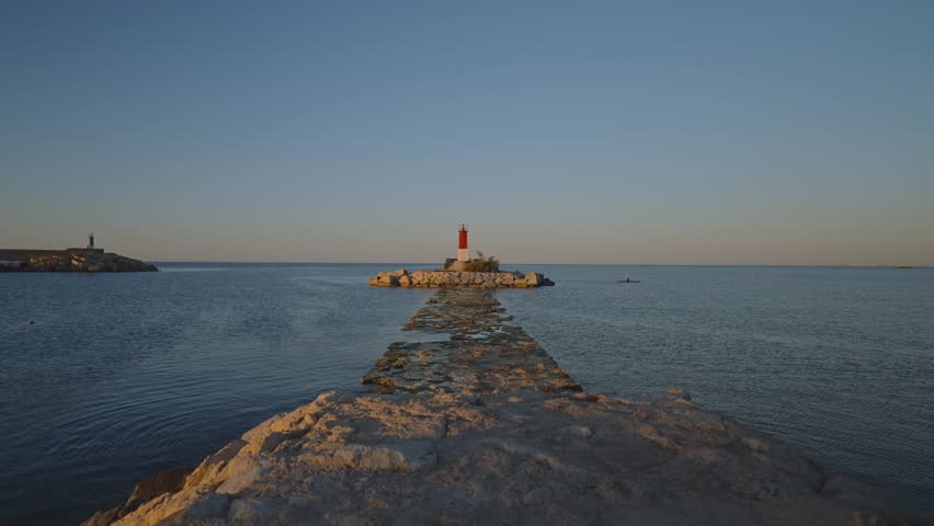 This takes the viewer through the Villajoyosa coast in Spain at sunrise. The video shows a pathway leading to a lighthouse and the clear water around it.