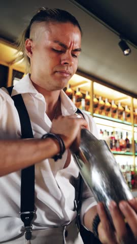 Young handsome mixologist preparing a delicious alcoholic beverage in a trendy bar. A professional bartender working with concentration