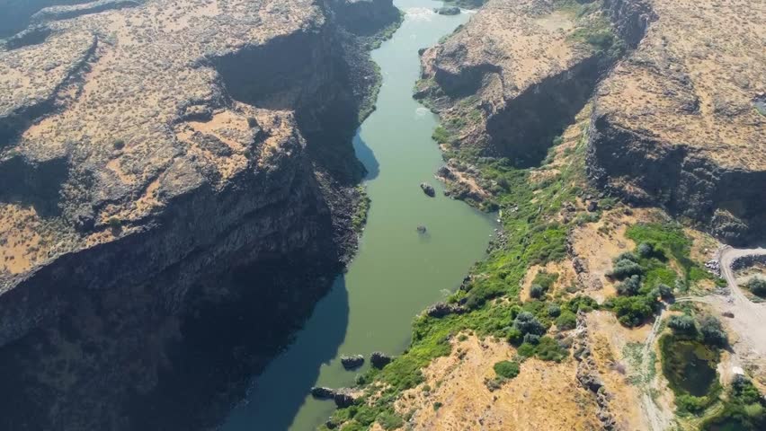 Dramatic aerial drone footage plunges into the deep Snake River Canyon near Twin Falls, Idaho, revealing towering basalt rock walls and the river threading through the narrow gorge below. The scale of this geological wonder — carved by ancient Bonneville floods — is breathtaking from the air. Perfect for geology, adventure travel, and Idaho landmark content.