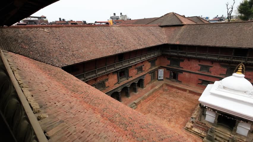 View of a traditional Newari courtyard with red brick architecture and a white stupa in Nepal.