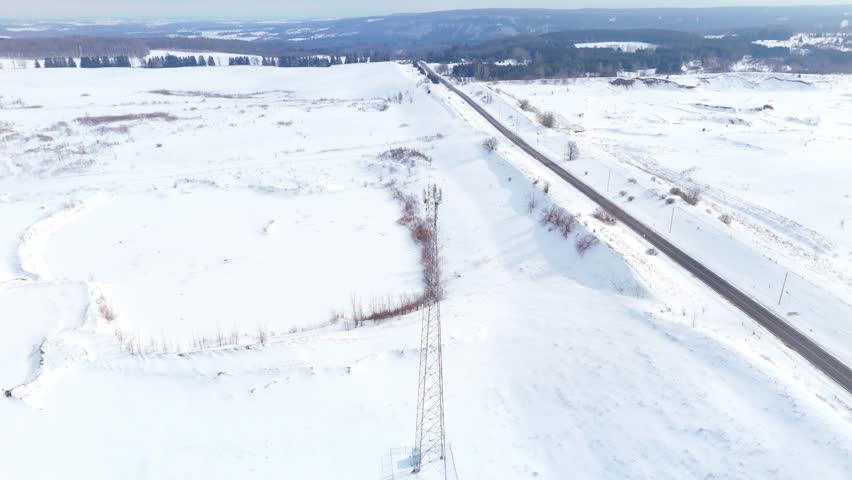 A tall telecommunication tower stands amidst a snow-covered expanse with a road running alongside. Ideal for use in technology or infrastructure-related content.