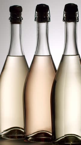 Three elegant bottles of rose and white sparkling wine rotating in slow motion, isolated on a clean white background, Elegant trio of sparkling wine bottles, featuring white, rose varieties, vertical