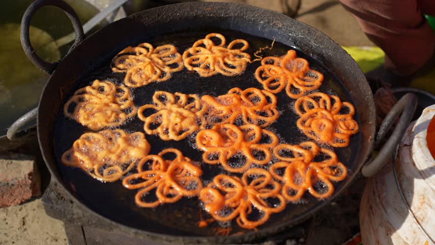 View of traditional jalebi sweets being deep-fried in a large pan of bubbling oil at a street food stall in Nepal.