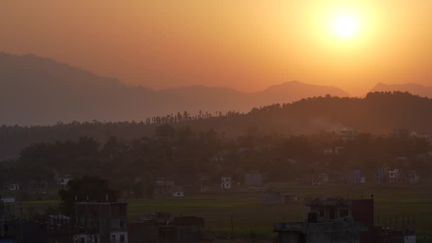 View of sunset over a valley town with hazy mountains and golden sky in Nepal.