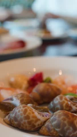 A close-up shot of sea snails and shrimp on a white plate at a buffet