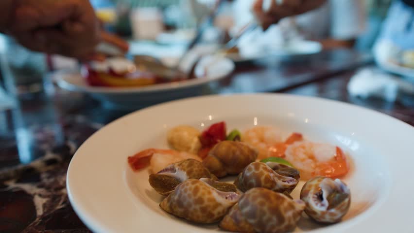 A close-up shot of sea snails and shrimp on a white plate at a buffet