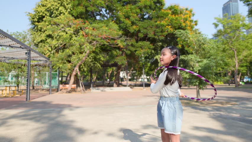 A happy Asian girl in pigtails plays with a hula hoop in a sunny park