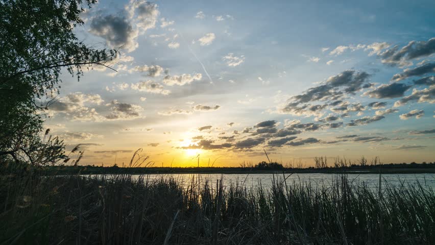 Sunset over a lake with beautiful clouds, timelapse of quickly flying clouds in the sky and the setting sun behind the horizon