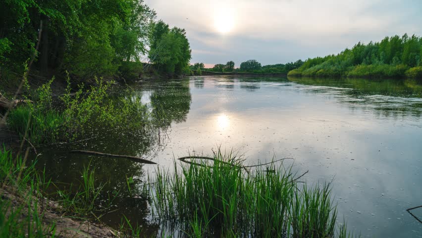 Sunset over a lake with beautiful clouds, timelapse of quickly flying clouds in the sky and the setting sun behind the horizon