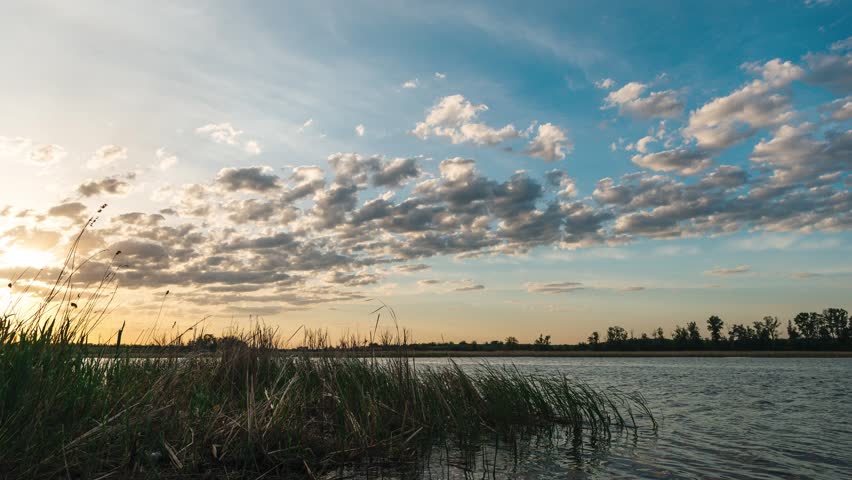 Sunset over a lake with beautiful clouds, timelapse of quickly flying clouds in the sky and the setting sun behind the horizon