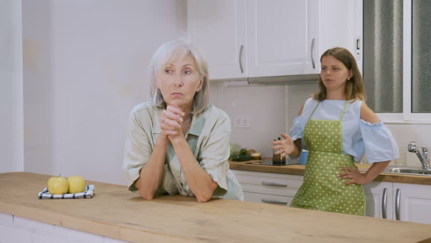 Offended young woman listening her senior mother standing behind and quarreling with her.