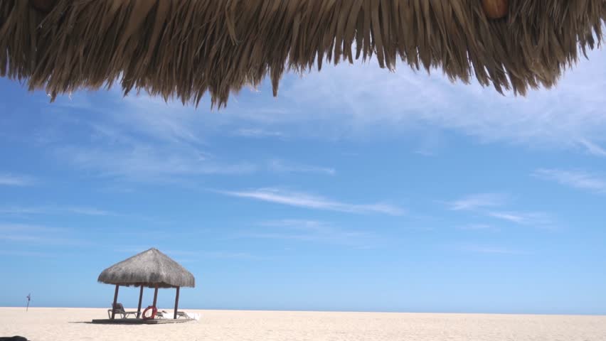 Sunny beach landscape with thatched umbrella on sandy shore, blue sky and peaceful tropical coastline with empty relaxation area