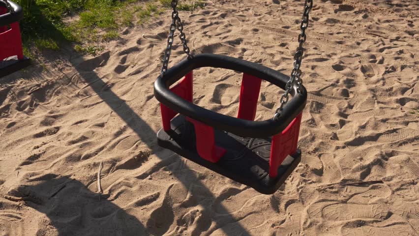 Empty Red and Black Child Swing Set Resting on Sandy Playground Ground Daytime Outdoor Recreation