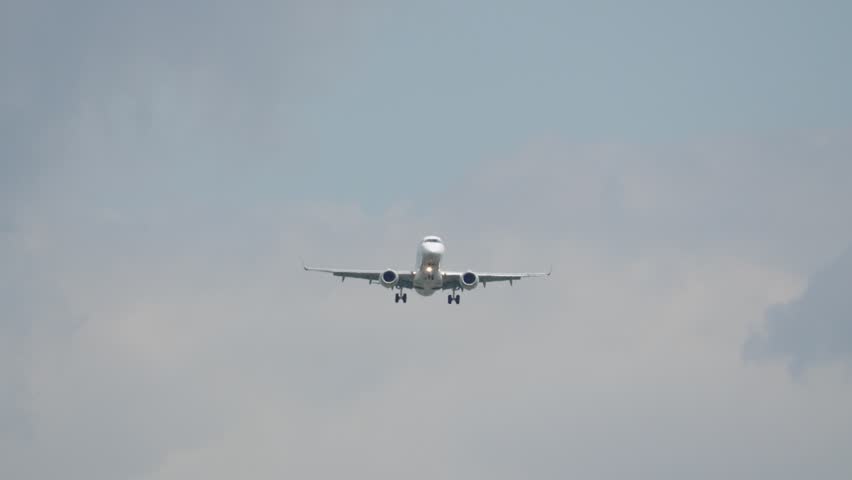 A commercial airplane descends towards the runway. The aircraft is in the final approach phase. The sky is mostly clear with few clouds.