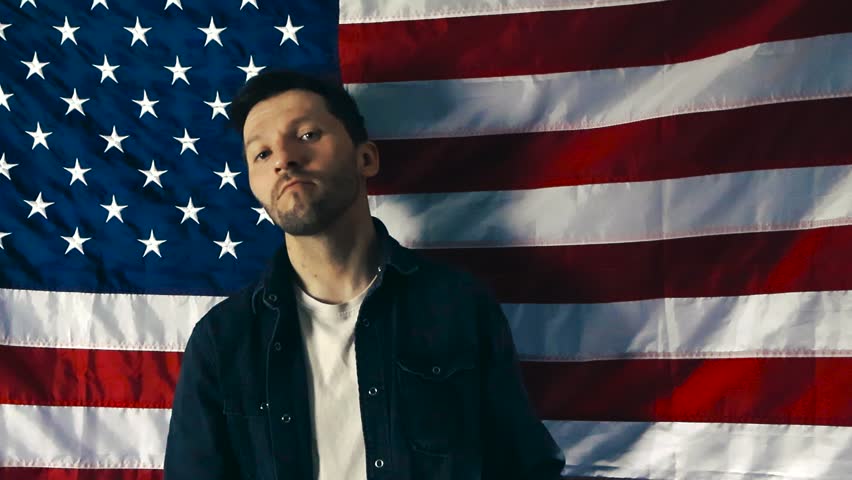 Young patriotic American man holding a sign for the 2026 midterm elections. The protestor is campaigning in front of the USA flag
