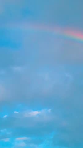Vibrant rainbow shining brightly in a blue, cloudy sky. A beautiful weather phenomenon appearing in the atmosphere after a summer rain