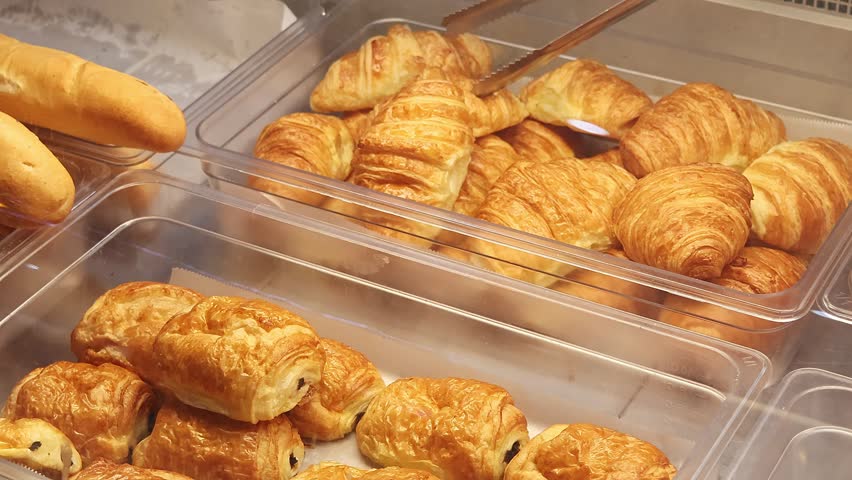 Customer choosing fresh croissant in bakery display, traditional French pastry selection in cafe or bread shop. Close up of golden brown flaky breakfast pastry, freshly baked buns.