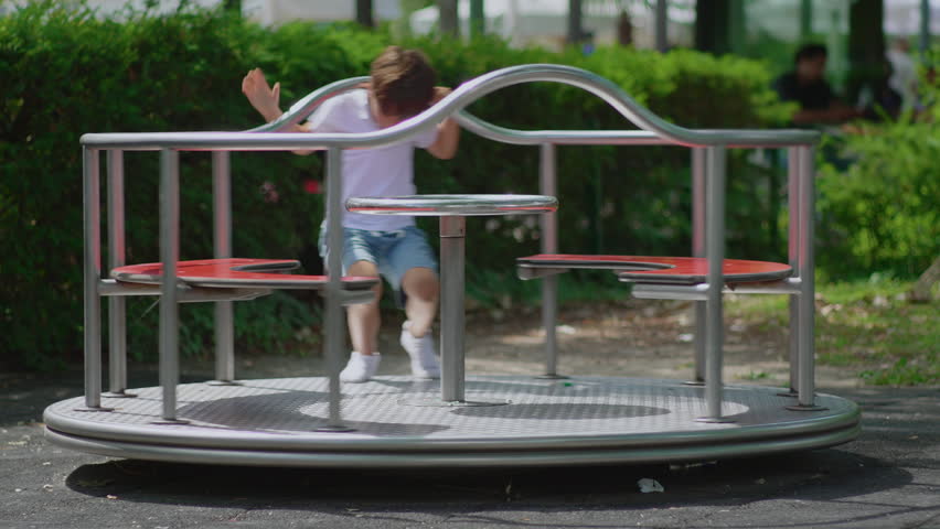Child riding merry go round while gripping metal handle and turning platform, lively playground scene showing excitement coordination and active play