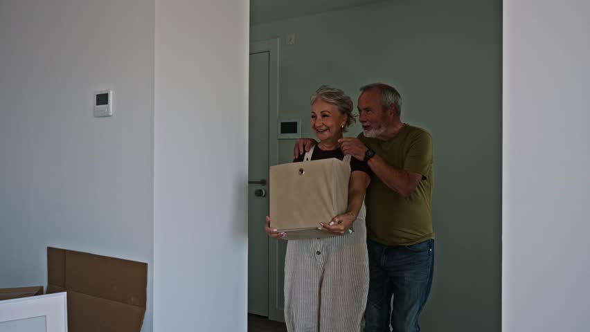 Happy senior couple entering their new apartment for the first time. The man and woman are carrying boxes and exploring their future home
