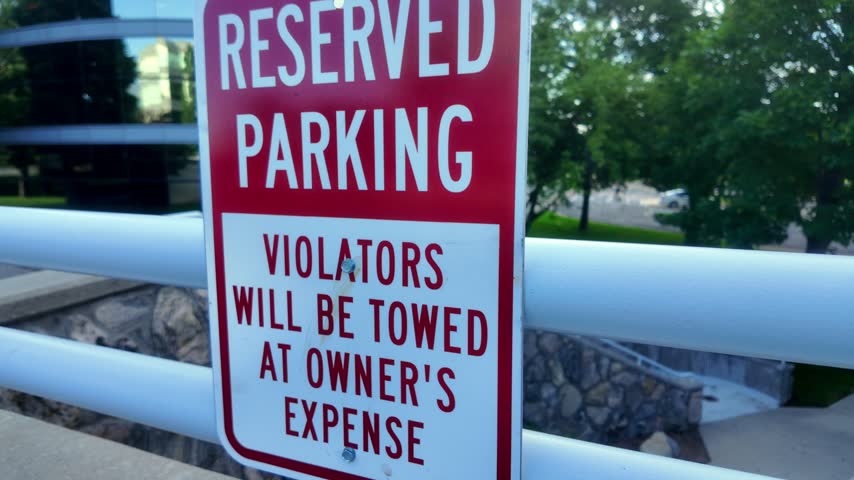 Reserved Parking Violators Will Be Towed At Owner’s Expense Red and White Sign with Business Complex Buildings in background uneasy feeling side angle view