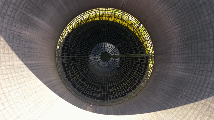 Vertical look down inside nuclear cooling tower, rusted grid and dark core center. Ecology issues and environmental impact of abandoned energy infrastructure. Central opening, steel grid layers and