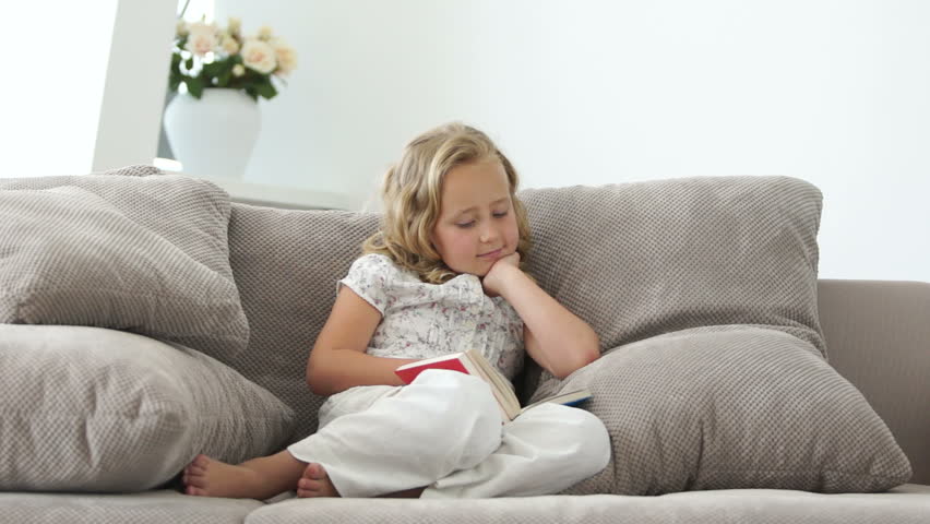 Child sitting on a sofa and reading a book
