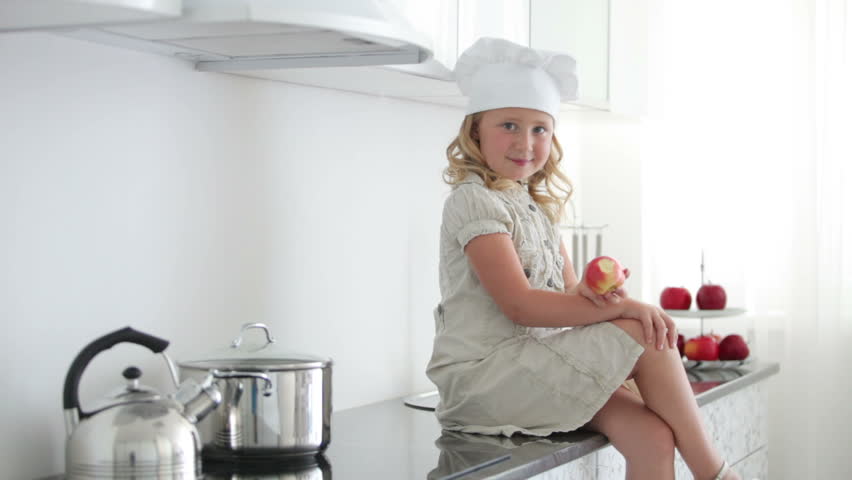 Cook girl sitting on the table and biting an apple
