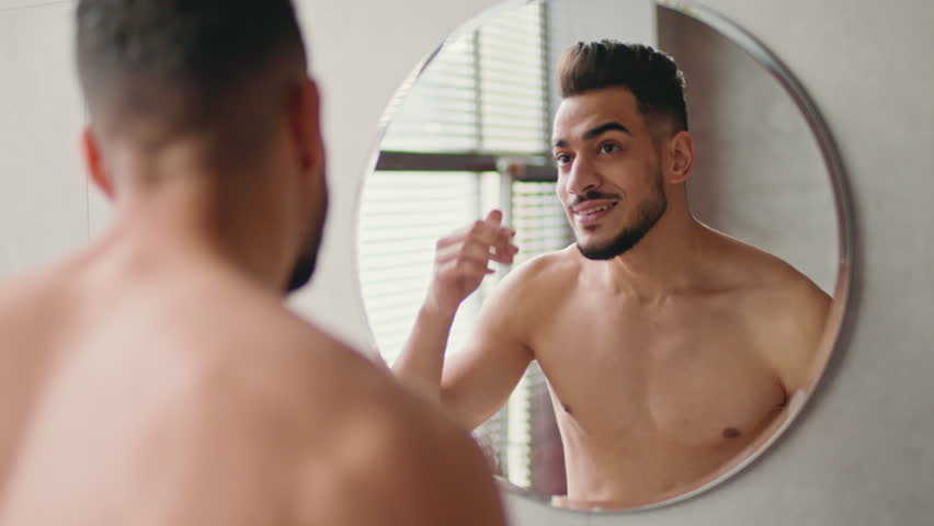 Young Man Styling Hair in Bathroom Mirror With Happy Expression