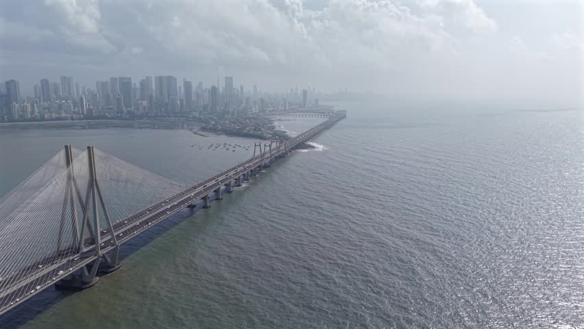 High angle aerial view of the Bandra-Worli Sea Link cable-stayed bridge with moving traffic, featuring the Worli city skyline and the Arabian Sea in Mumbai, India.