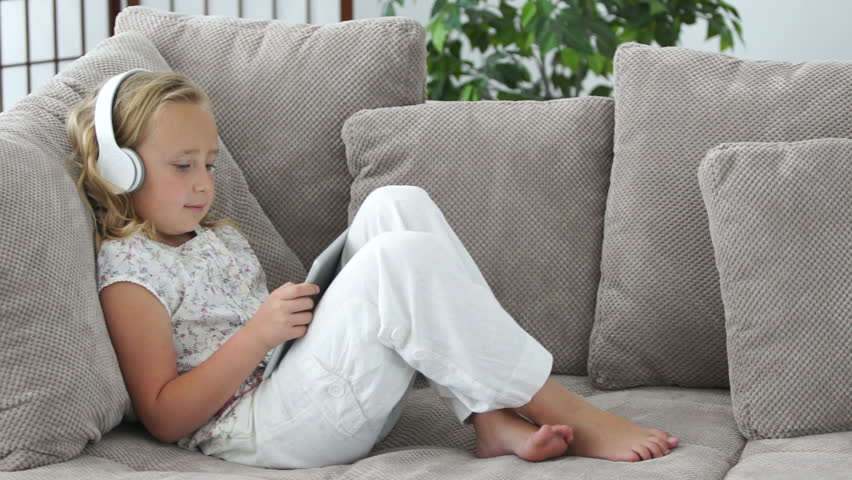 Girl lying on couch with tablet pc and listening to music
