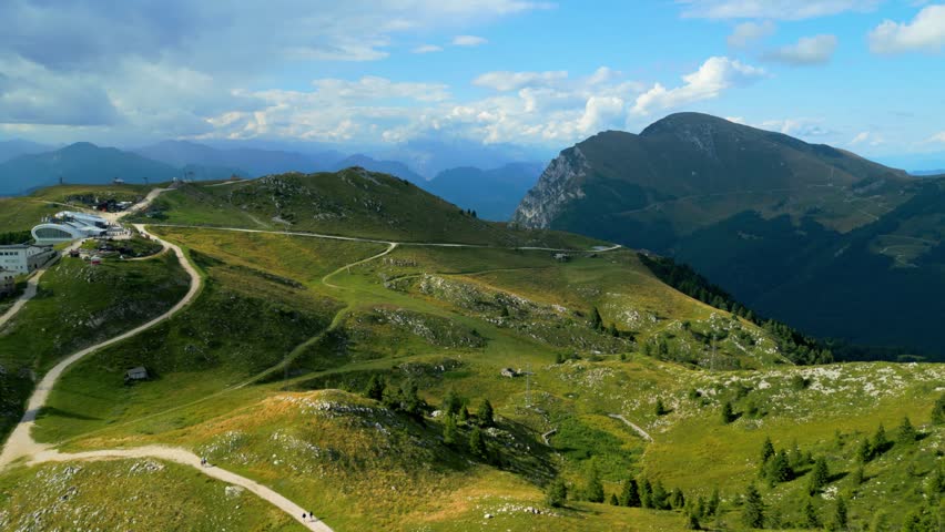 Wide aerial view of grassy mountain slopes, hiking paths, and rugged alpine landscape