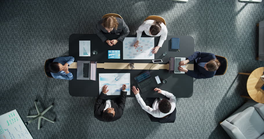 Top Down View of Business Professionals Collaborating Around Office Table With Laptops and Charts as Linked Visualization Layer Appears, Glowing Blue AI Icons Represent Data Analytics and Security.
