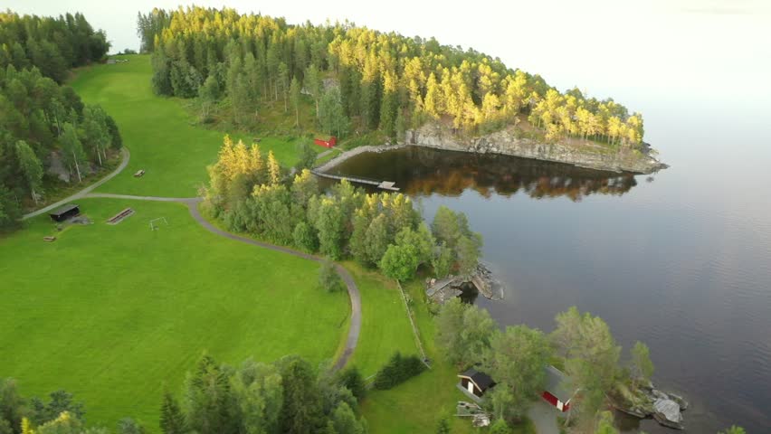 Aerial drone footage of a small forested peninsula reaching into a calm Norwegian lake with early autumn colors in central Norway.