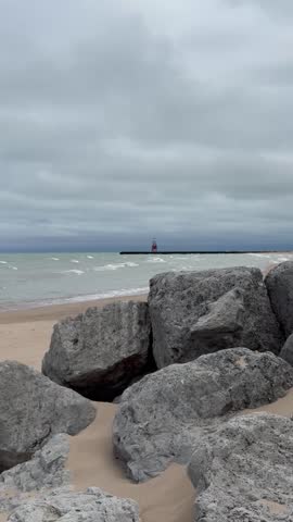 4K vertical video of a sandy Chicago beach on Lake Michigan with rocks, a lighthouse, and gentle waves washing over the shoreline