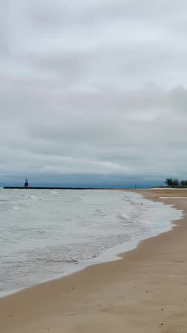 4K vertical video of a sandy beach in Chicago on Lake Michigan with a lighthouse and gentle waves rolling onto the shore