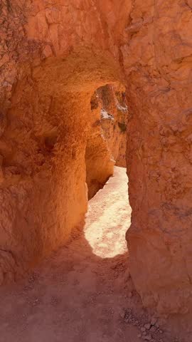 First person perspective walking through a narrow canyon arch on the navajo loop trail revealing the stunning hoodoos and red rock formations of bryce canyon national park in utah on a sunny day