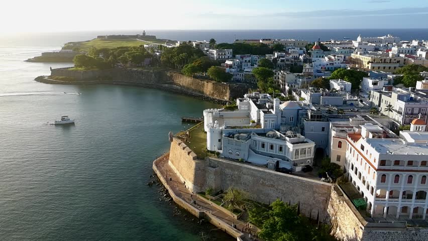 Drone video during sunset of one of the city walls at old San Juan, Puerto Rico showing the bay, tourist, homes, buildings and Morro Castle.