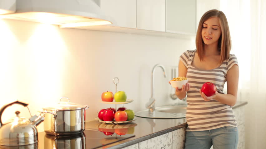 Girl holding an apple and bowl with corn flakes
