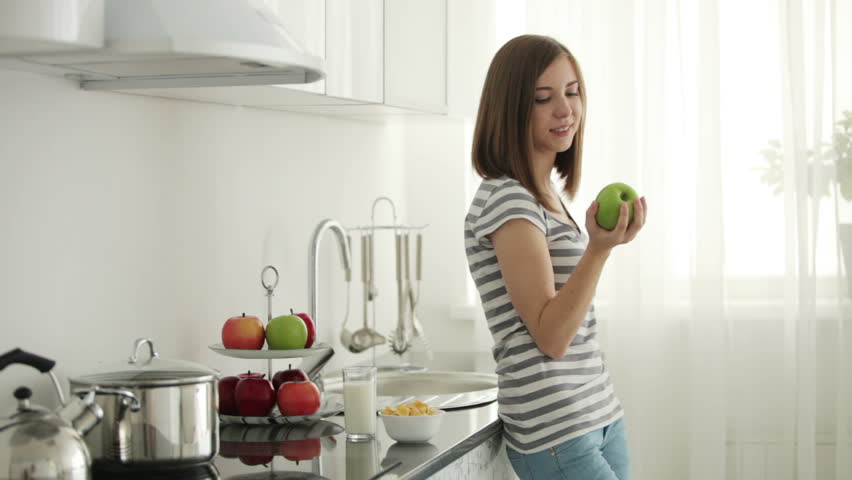 Cute girl standing in kitchen and bitting apple
