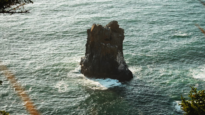 Cannon Beach, Large sea stack rock rising from ocean waves along rugged coastline under daylight