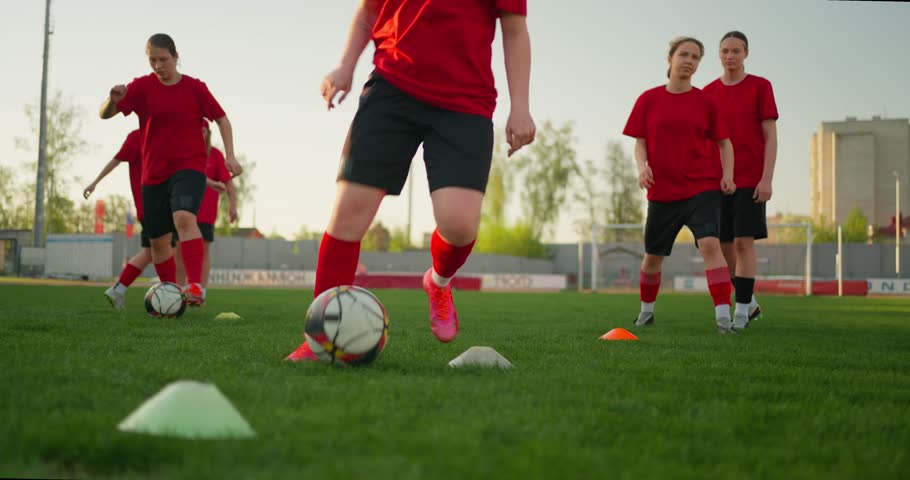 Youth soccer players in red uniforms practice dribbling drills around cones on a sunny outdoor field during team training session