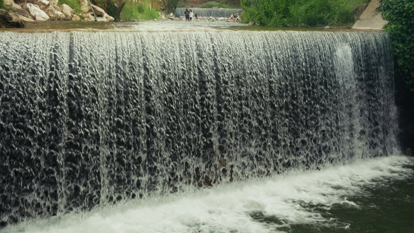 Wide scenic shot of a powerful waterfall cascade flowing into a rocky river bed with fresh water streaming over large wet stones and boulders in a crisp high fidelity beautiful natural mountain landscape texture
